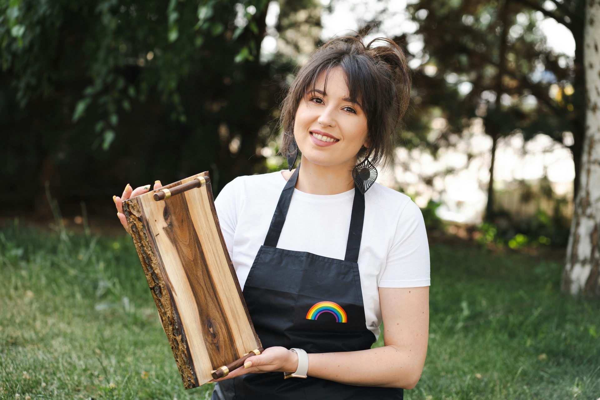 Woman holds firewood outdoors, smiling at the camera.